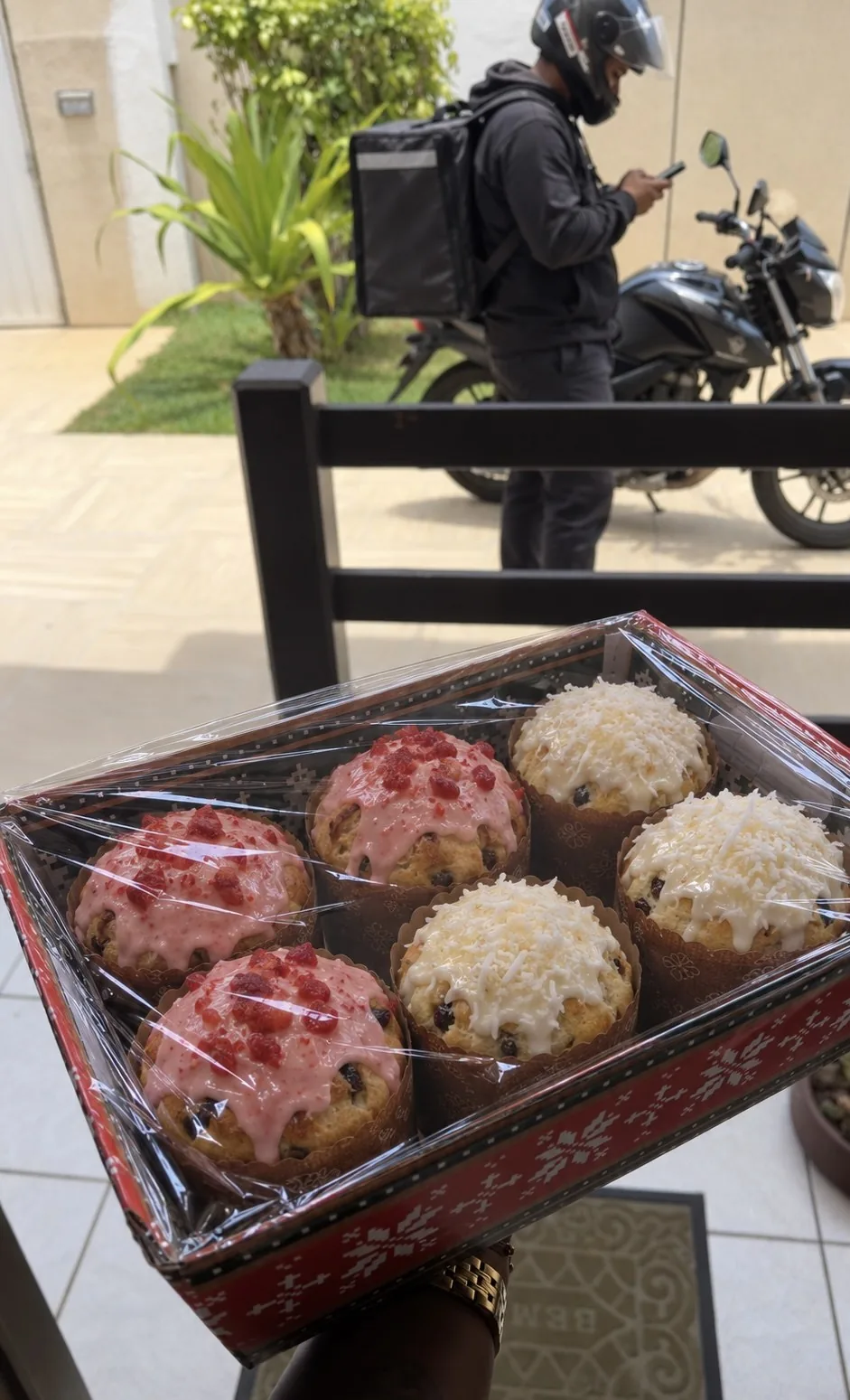 Caixa de mini panetones na mão, com o motoboy ao fundo